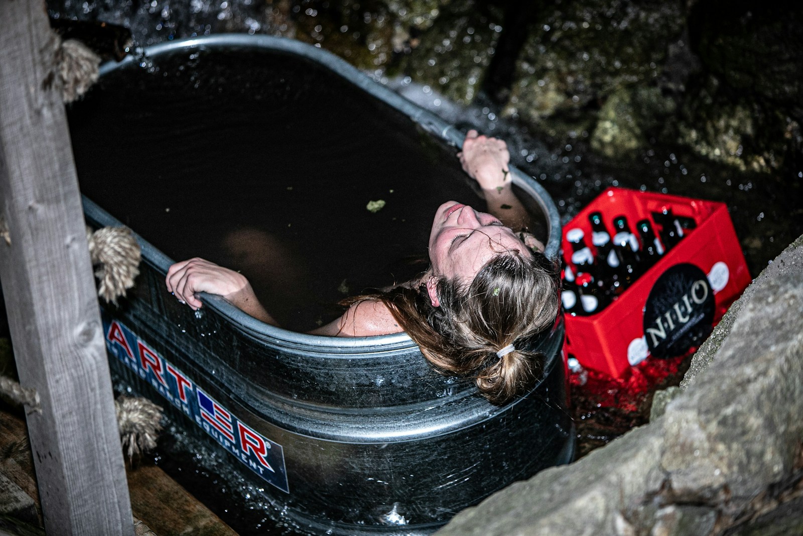 A home recovery setup showing a cold plunge tub, a small sauna, and a pair of pneumatic compression boots arranged in a garage