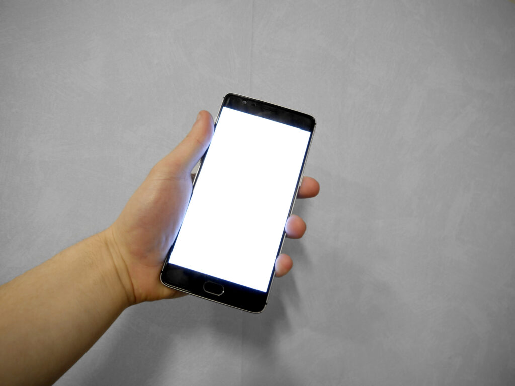 Main tenant un t&eacute;l&eacute;phone allum&eacute; au bord d'un banc, sac de sport au premier plan