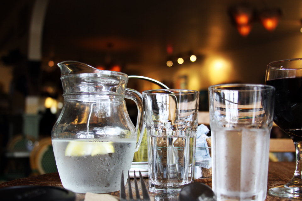 Verre d'eau rempli posé sur une table en bois près d'une fenêtre lumineuse
