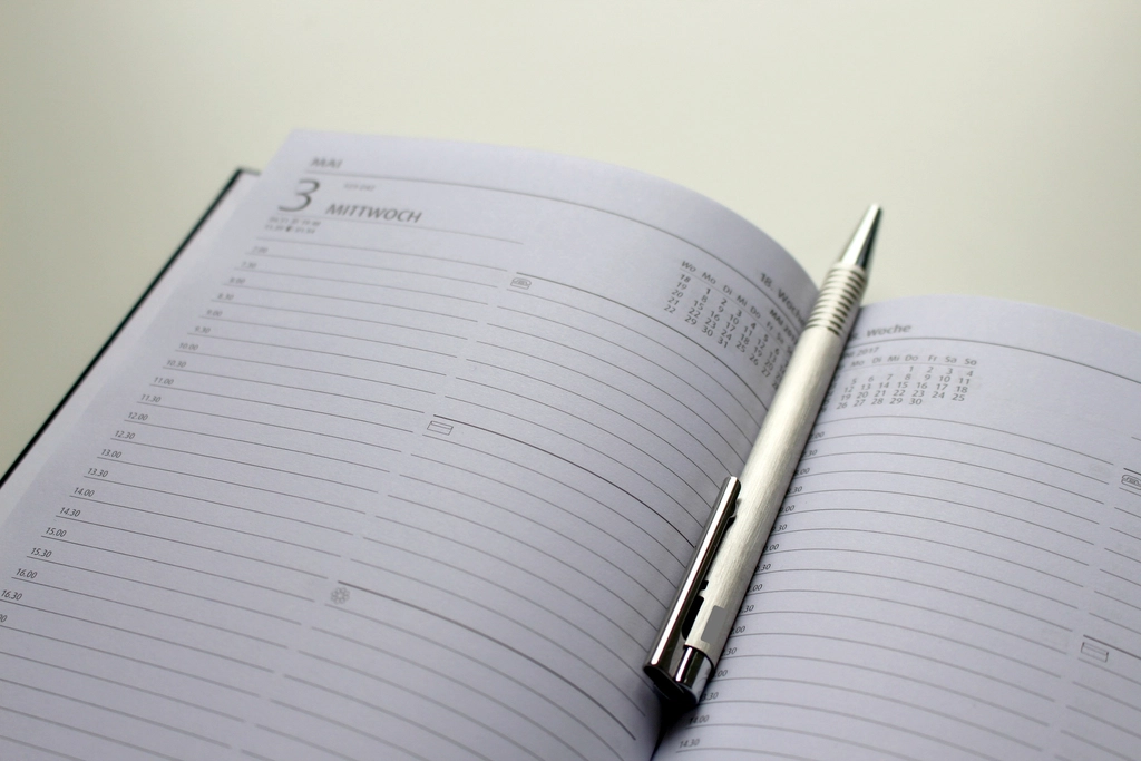 Page de calendrier hebdomadaire annotée au stylo, posée sur un bureau en bois