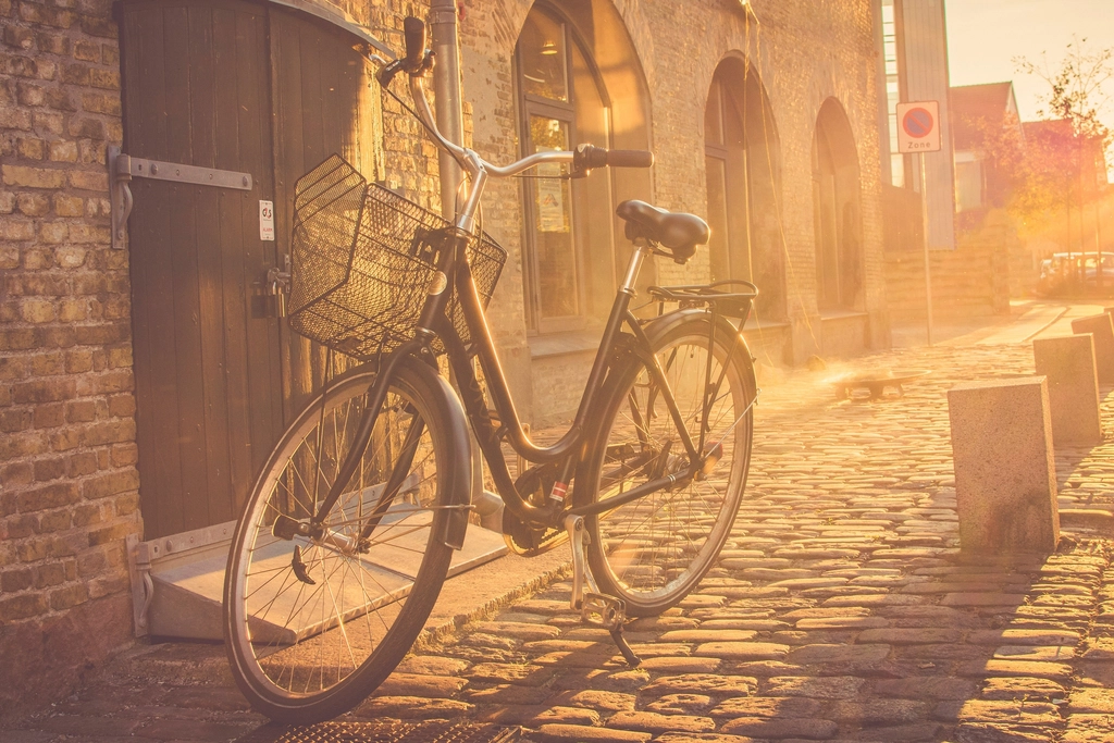 Vélo attaché à un poteau sur un trottoir en fin de journée, ville à l'arrière-plan