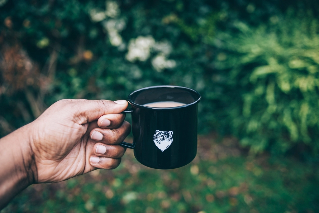 Tasse de café noir posée sur une table en bois près d'un carnet ouvert