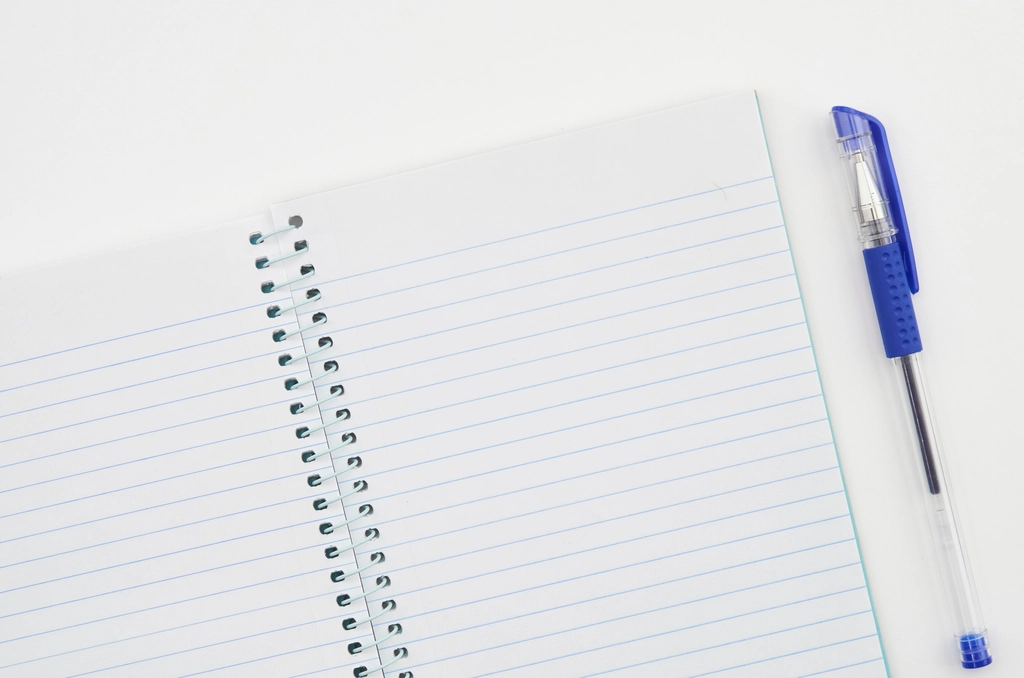 Carnet ouvert avec un stylo posé dessus sur une table en bois clair
