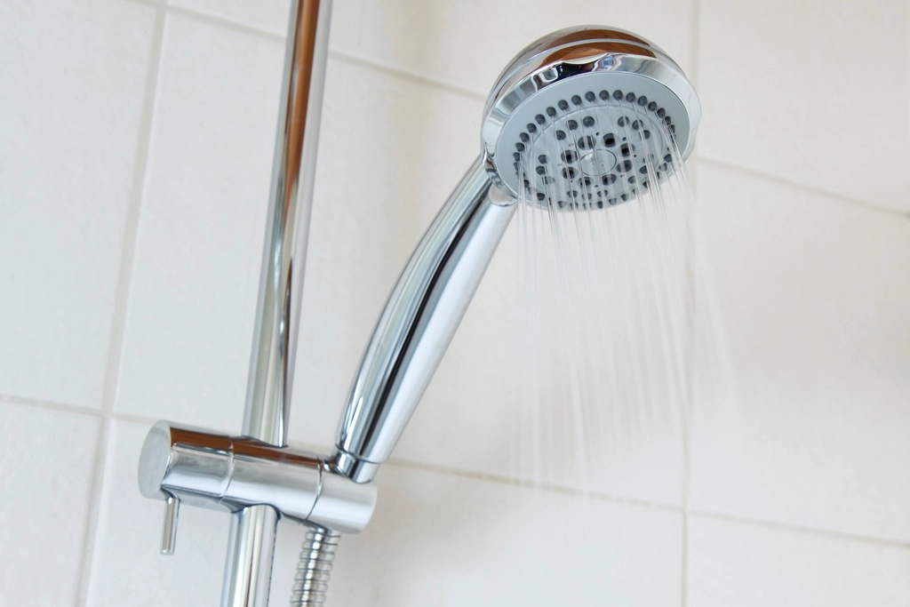 Pommeau de douche laissant couler un jet d'eau dans une salle de bain simple